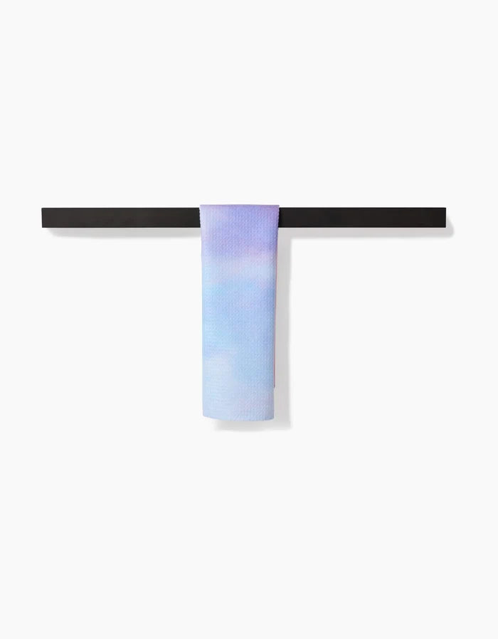 The Magic In The Sky Bar Towel by Stefanie Bales, featuring pastel blue and lavender Geoweave™ fabric, is draped over a minimalist black towel rack against a plain white background.