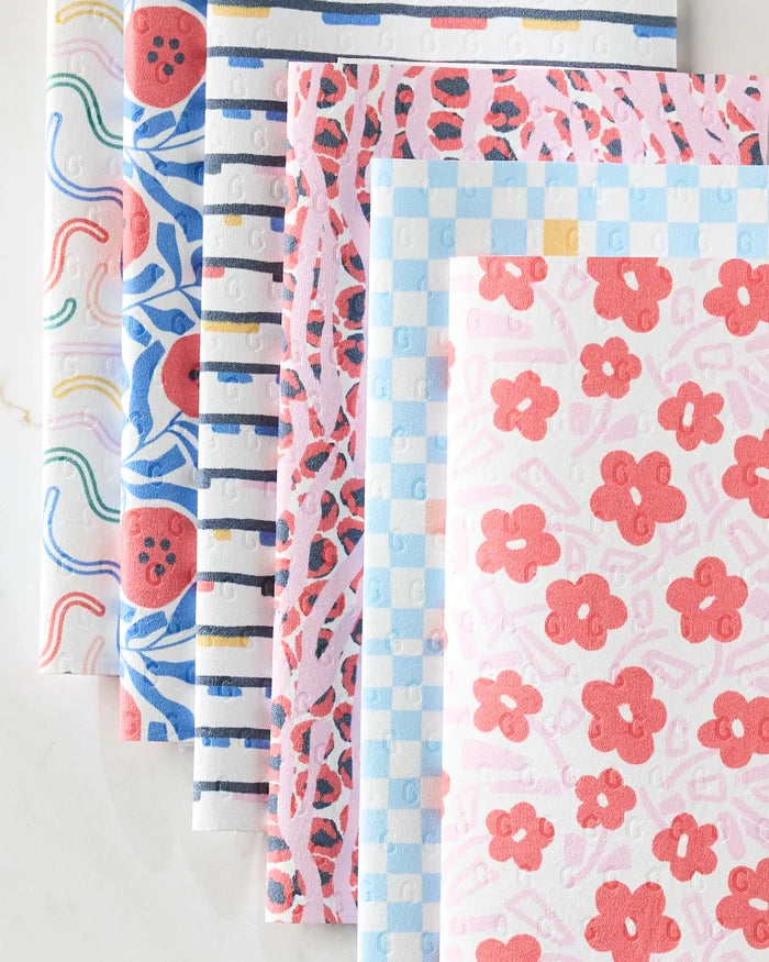 The Happy Hemera Magic Wand is an eco-friendly set of six dish towels featuring colorful florals, stripes, checks, and abstract patterns—a vibrant alternative to paper towels, neatly stacked on a white surface.