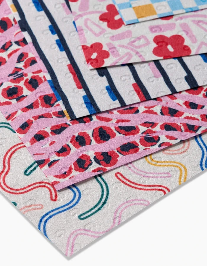 A close-up of stacked Magic Wand squares by Happy Hemera, made from recycled materials and featuring colorful floral, animal, striped, plaid, and curved designs on a white background.