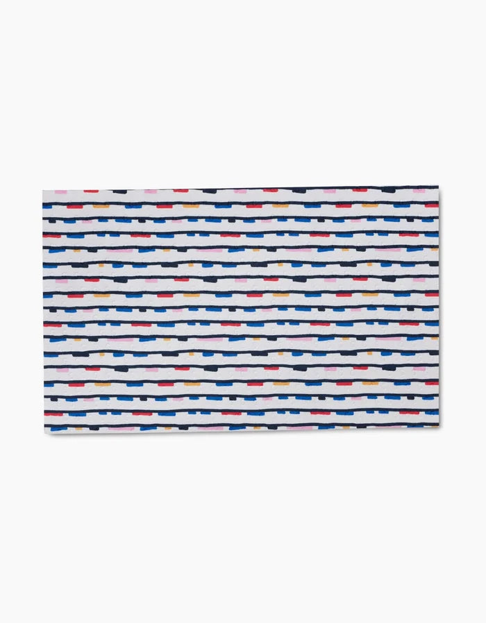 The Happy Hemera Magic Wand features a rectangular shape with a white background and horizontal rows of irregular, short dashes in navy blue, red, gold, and pink. Crafted from recycled materials for an eco-friendly touch and modern style.