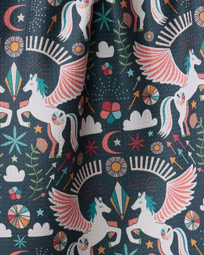 Add magic to your kitchen with the "Magical Moments" tea towel by Jessica Swift, featuring white winged unicorns, flowers, stars, moons, and more in vibrant patterns on a dark background.