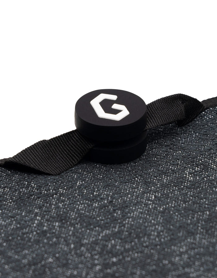 Close-up of Magna - Blue Palms by GEOMETRY: a black, textured ultra-absorbent towel with a round black button featuring a white G logo, attached by a black ribbon loop.