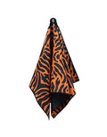 A GEOMETRY Magna - Tiger fitness towel, featuring an orange and black tiger stripe pattern and made from recycled materials, hangs from a hook against a white background.