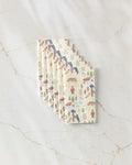 Six folded Elisabeth Wing "Mama Bear" cloth napkins, featuring a vibrant outdoors-themed bear and nature print, stacked neatly on marble—a stylish, eco-friendly alternative to paper towels.