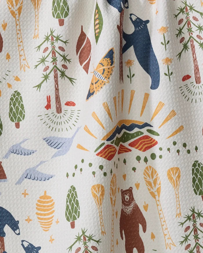 The Mama Bear dish towel by Elisabeth Wing features bears, birds, trees, beehives, leaves, and a sunburst over mountains in earthy green, yellow, blue, and brown tones—an inviting touch for any kitchen.