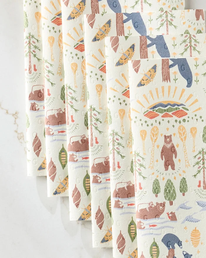 Eight eco-friendly Mama Bear paper towels by Elisabeth Wing, each with nature-themed designs—bears, trees, fish, pine cones, paddles, and a sun—in earthy greens, browns, blues, and yellows on a white background.