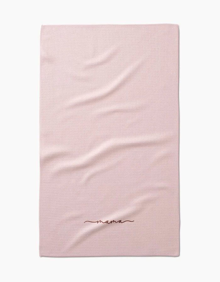 The Kailee Wright Mama blanket is light pink with a textured, ultra-absorbent Geoweave fabric and mama embroidered in dark red cursive near the edge. It’s shown laid flat with a few gentle folds.