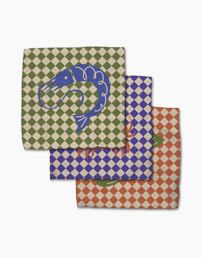 Three Mar napkins by Geometry overlap on a white background, each with a unique checkered color (green, blue, orange) and seafood illustration like shrimp—crafted from durable Geoweave fabric for superior dishcloth performance.