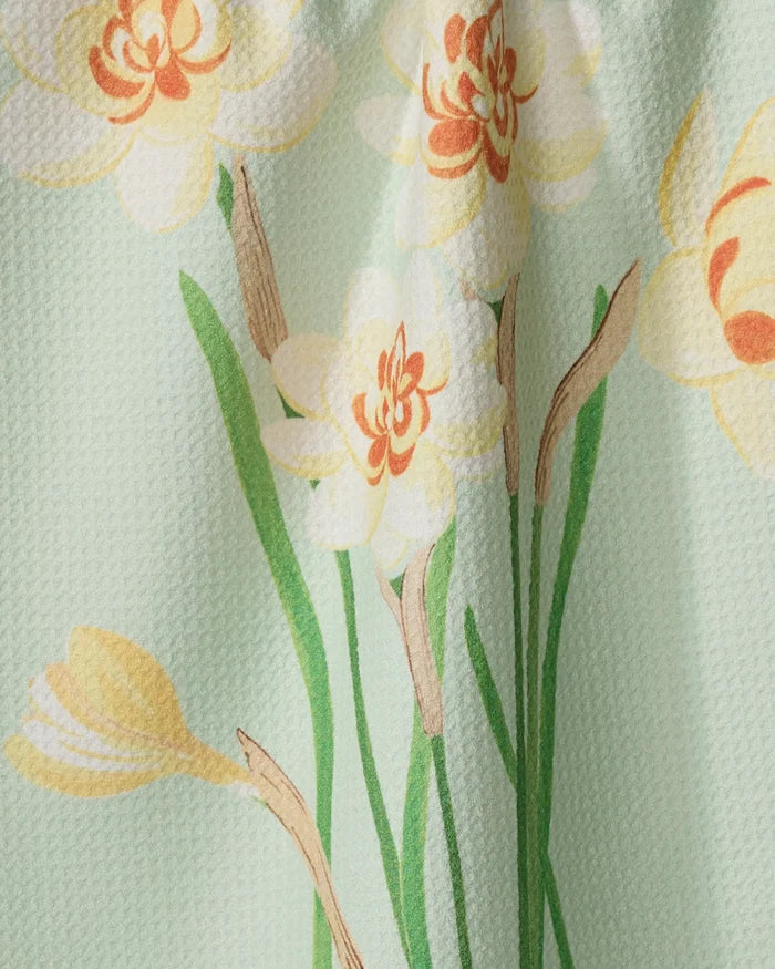 A close-up of the Linda Fox "March Daffodils" recycled kitchen towel, showing its textured surface and floral print with yellow and orange daffodil-like flowers and green stems on a pastel green background.