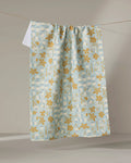 The Elisabeth Wing "March" tea towel, ultra-absorbent in light blue with a yellow floral and vine pattern, hangs on a clothesline against a neutral background.