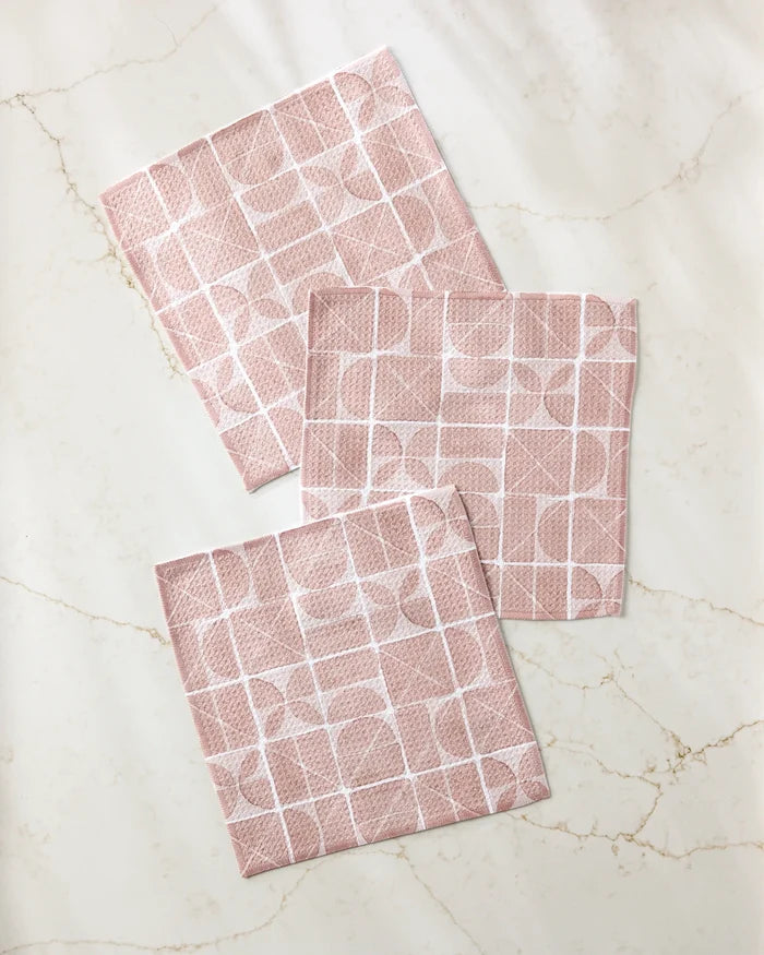 Three Mariposa napkins by Studio Jeannot, crafted from recycled materials in pink with a white grid and semicircle pattern, are displayed on a light, marble-like surface.