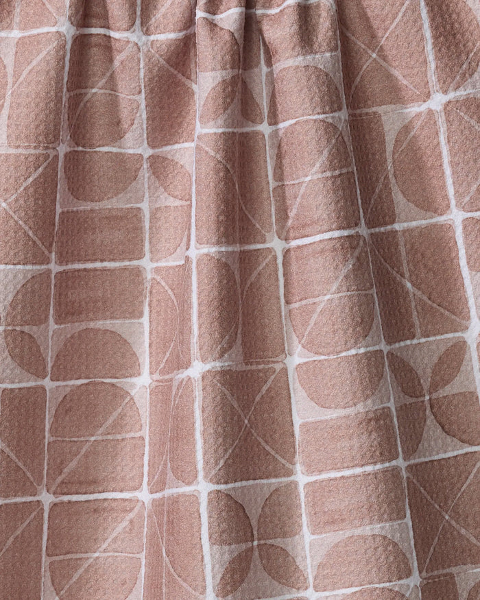 A close-up of Mariposa by Studio Jeannot, a tea towel featuring pinkish-beige fabric with a textured surface and a grid-like geometric pattern of white lines, circles, semi-circles, and rectangles—an elegant kitchen essential.