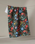 The Danelys Sidron "Marsh Wren" kitchen towel, featuring an eco-friendly design with a vibrant red, blue, yellow, and green floral pattern, hangs on a clothesline against a neutral background.