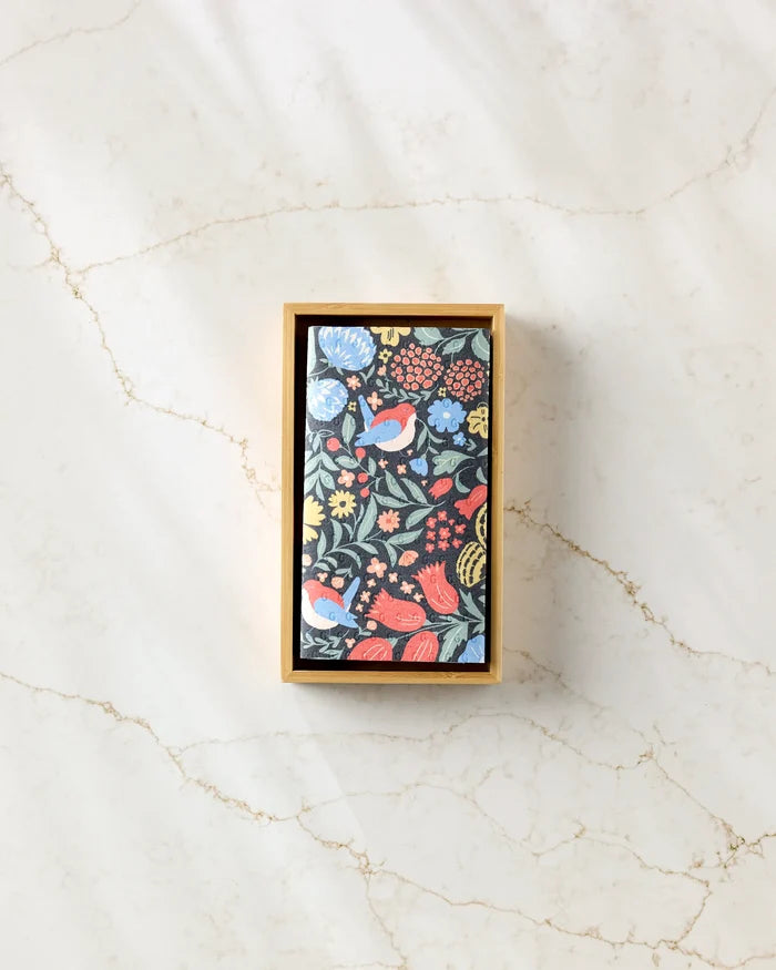 The Marsh Wren by Danelys Sidron is a rectangular box with a lid decorated in colorful floral and bird patterns, designed for reusable paper towels. It sits on a light marbled surface and is viewed from above amid soft shadows.