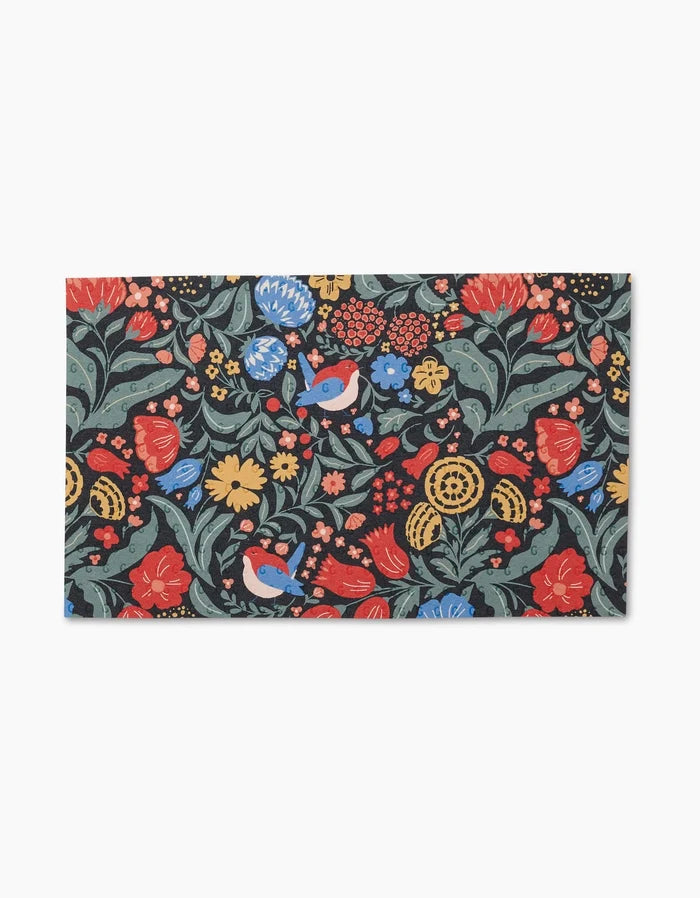The Marsh Wren mat by Danelys Sidron features a vibrant floral and bird pattern in red, yellow, and blue on a dark background. Made from eco-friendly post-consumer recycled materials. Not paper towels.