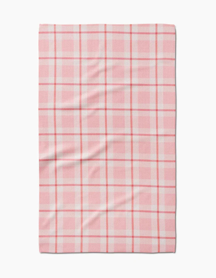 The Marva Lu tea towel by Kelsi Fullmer is rectangular, made from recycled materials, and showcases a pink and white plaid pattern with intersecting lines and gentle surface wrinkles.