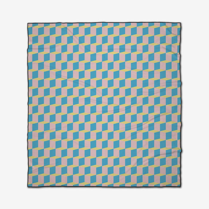The GEOMETRY “Math Class” beach blanket is quick-drying and features a striking, three-dimensional optical illusion of interlocking blue, yellow, and light pink cubes on a white background.