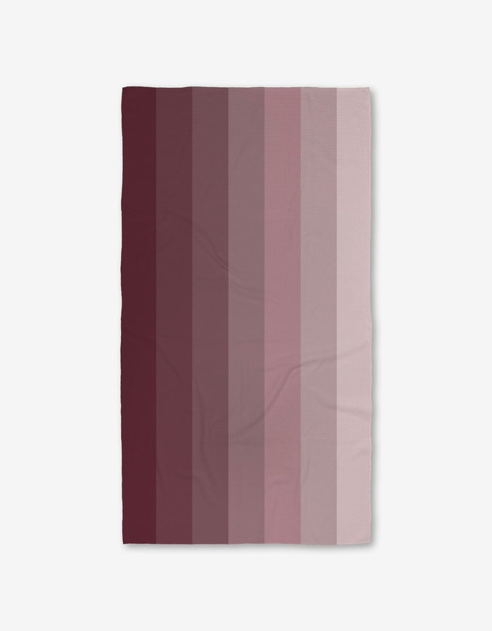The GEOMETRY Mauve Levels Bath Towel features vertical stripes blending dark maroon to pale pink on white, and its Geoweave technology ensures ultra-absorbency and style for your bathroom.