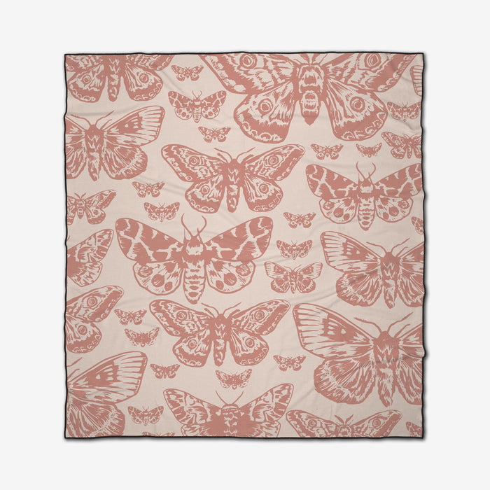 The GEOMETRY Mauvy Moths is a beige compact beach blanket made from recycled materials, featuring a repeating pattern of pink and rose-colored moth illustrations.