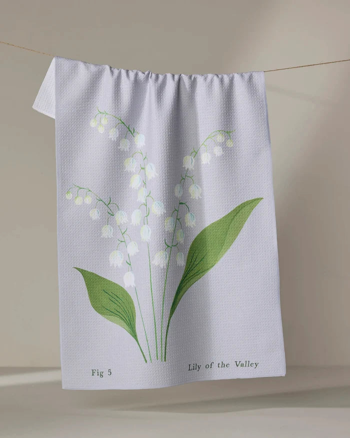 The Linda Fox "May Lily Of The Valley" is a white recycled tea towel featuring green leaves and delicate white flowers, with the text "Fig 5 Lily of the Valley," shown hanging on a clothesline.