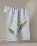 The Linda Fox "May Lily Of The Valley" is a white recycled tea towel featuring green leaves and delicate white flowers, with the text "Fig 5 Lily of the Valley," shown hanging on a clothesline.
