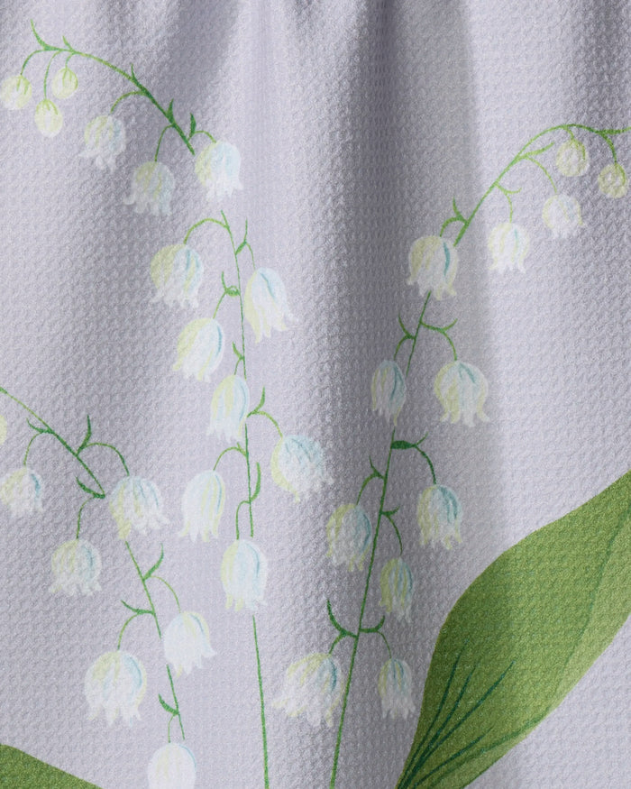 Close-up of the "May Lilly Of The Valley" tea towel by Linda Fox, made from quick-drying white fabric and printed with green leaves and delicate white lily of the valley flowers.