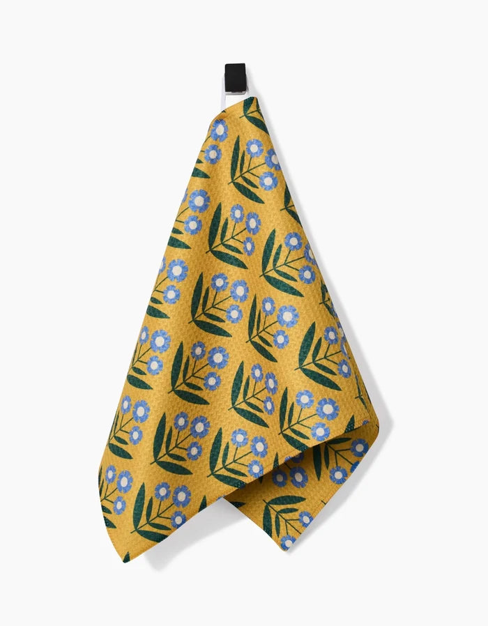 The Mayday Bar Towel by Megan Kampa features a yellow design with blue flowers and green leaves, hangs from a black loop against a white background, and is crafted from recycled materials.