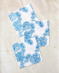 Three Meadowline napkins by Second Nature Studio, featuring blue floral patterns on white and made from recycled materials, are arranged with overlapping corners on a light marble surface.