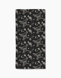 The Meow or Never bar towel by Cole Strem is a black, rectangular towel made from post-consumer recycled materials. It features white line art tattoo motifs—CATS hearts, birds, stars, moons, and flowers—on repeat.