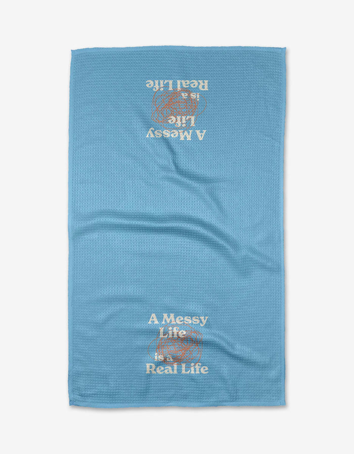The Messy Life tea towel by Quotes by Christie is blue with a textured Geoweave fabric and “A Messy Life is a Real Life” printed in white and beige, upright at the bottom and upside down at the top.