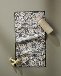 A beige water bottle and small beige dumbbells rest beside the GEOMETRY Metro Mesh ultra-absorbent black and white fitness towel on a flat, light gray surface.