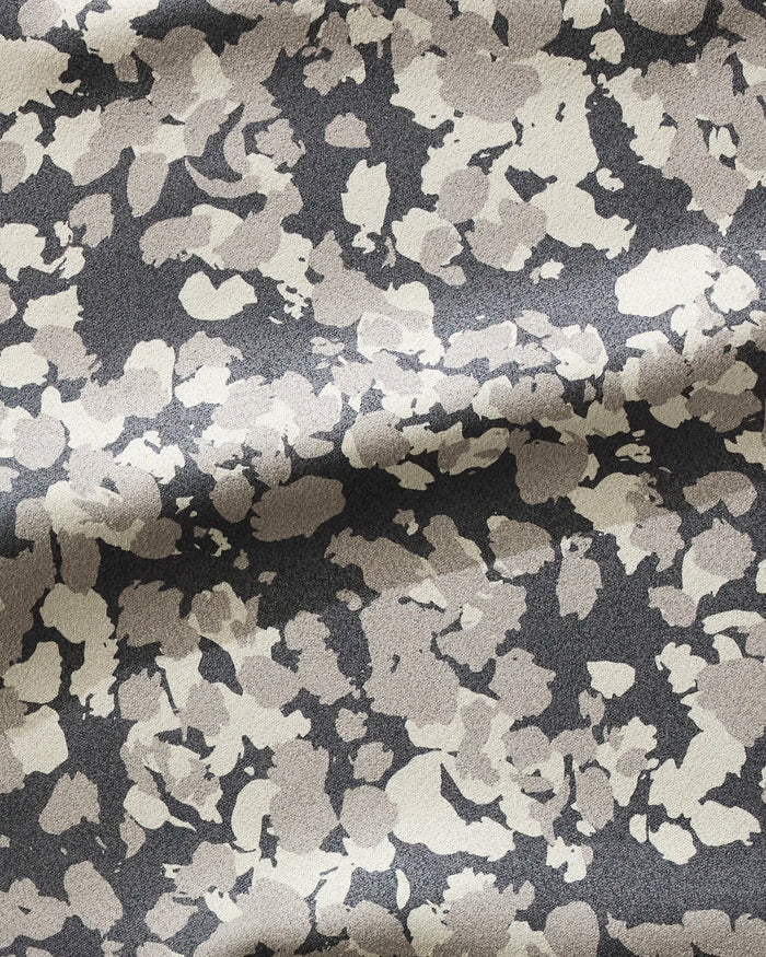 A close-up of GEOMETRY’s Metro Mesh fabric, crafted from recycled materials, shows gentle folds and texture with a light beige and gray abstract spotted pattern on a dark background.