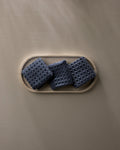 Three "Midnight Blue" waffle washcloths by GEOMETRY, made from recycled materials, are neatly displayed on a light oval tray atop a smooth taupe surface with gentle shadows.