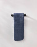 The GEOMETRY Midnight Blue luxury hand towel with a waffle texture is neatly folded over a sleek black towel bar on a white wall.