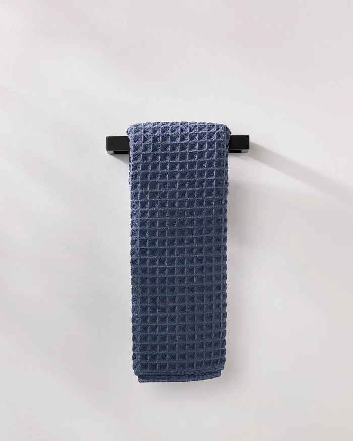 The GEOMETRY Midnight Blue luxury hand towel with a waffle texture is neatly folded over a sleek black towel bar on a white wall.