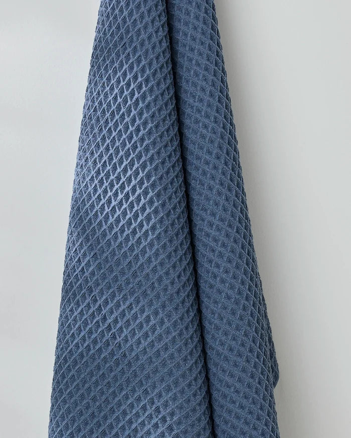 The GEOMETRY Midnight Blue waffle bath towel, with its textured finish, hangs against a white wall, bringing a touch of luxury to any bathroom.