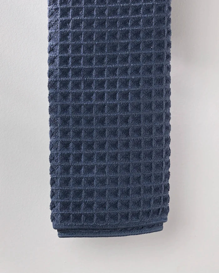 A neatly folded GEOMETRY Midnight Blue waffle hand towel with a textured weave hangs against a light gray wall.