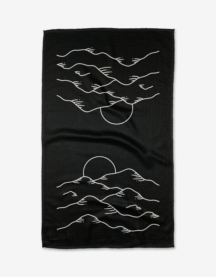 The Midnight Mountain Tea Towel by Graphics and Grain is black, made from Geoweave fabric, and showcases minimalist white line art of a sunset behind mountains and clouds, with the design repeated vertically.