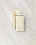 A stack of Mindful Mix colorful, patterned notebooks by Mindfulnice is fanned out on a white marble surface with veining, next to a neatly folded set of eco-friendly paper towels.