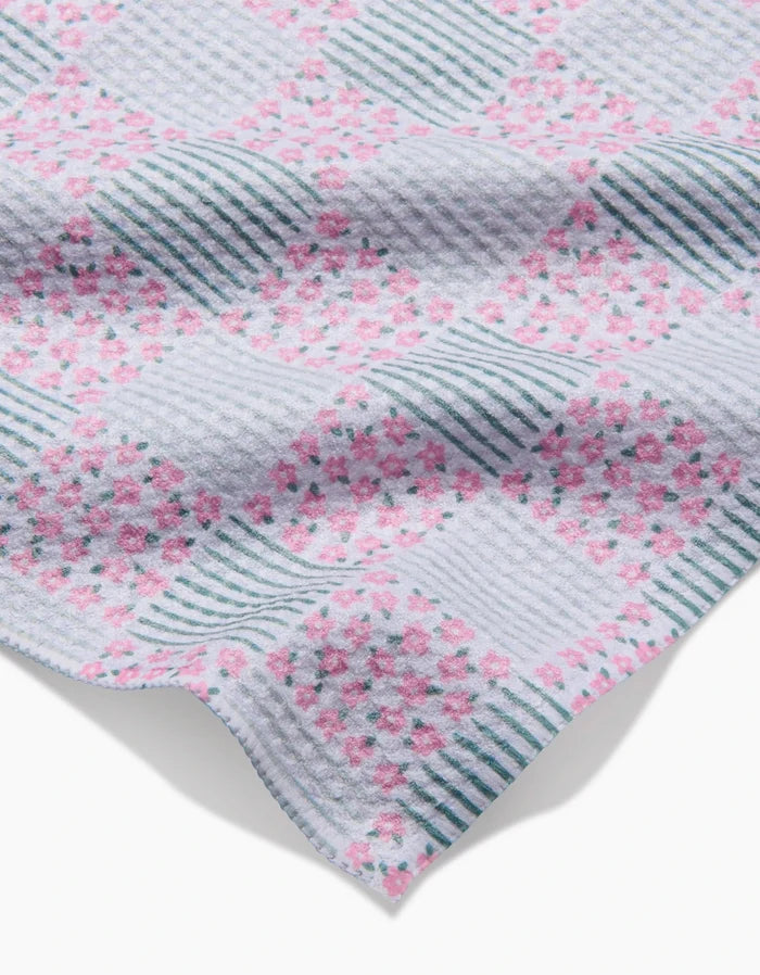 A close-up of Hufton Studio’s Mini Flowers and Stripes Check Pink and Green Bar Towel, crafted from Geoweave fabric, showing blue stripes and clusters of pink flowers on a white background, with a soft, textured look.