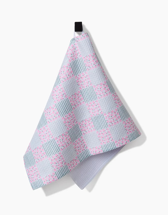 The Hufton Studio Mini Flowers and Stripes Check Pink and Green tea towel hangs from a black loop against a white background, featuring pastel pink and green checks crafted from Geoweave fabric for enhanced absorbency and durability.