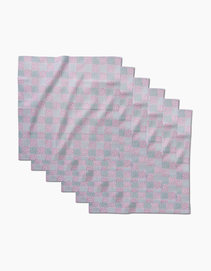 Seven rectangular placemats from Hufton Studio’s Mini Flowers and Stripes Check collection, featuring a pastel pink and blue checkered pattern, are arranged in a staggered, overlapping layout on a white background.