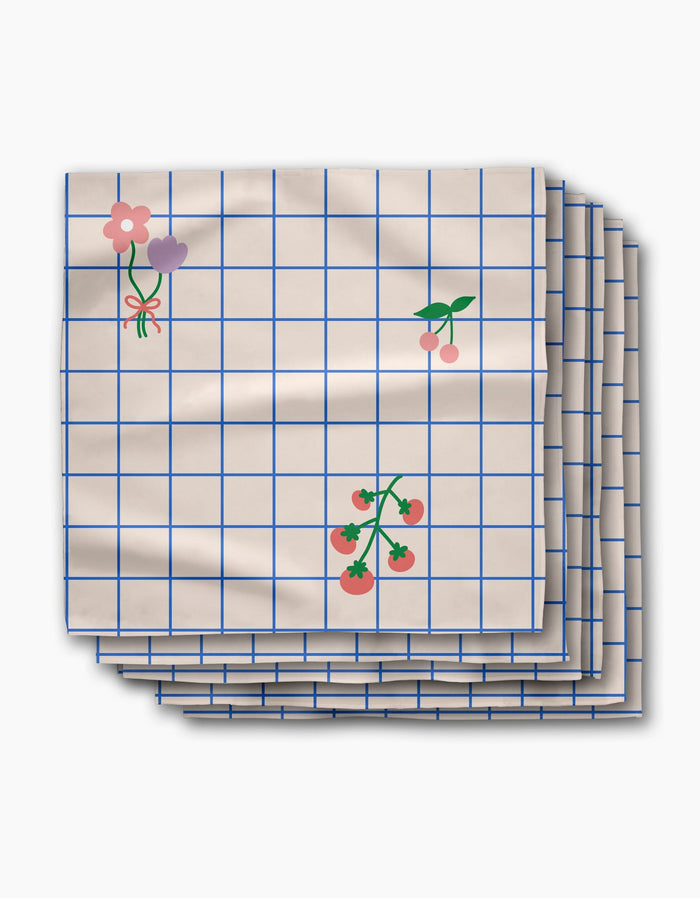 The Mini Harvest dinner napkin set by Letters By Shells features cream-colored Geosuede recycled fabric with a blue grid and charming flower, cherry, and tomato illustrations.