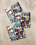 Three colorful napkins from Claire Iglesias’ Modern Bauhaus Mood set feature absorbent, recycled beige fabric with bold geometric and abstract patterns—green, blue, red, black, and pink shapes, lines, and eye motifs.