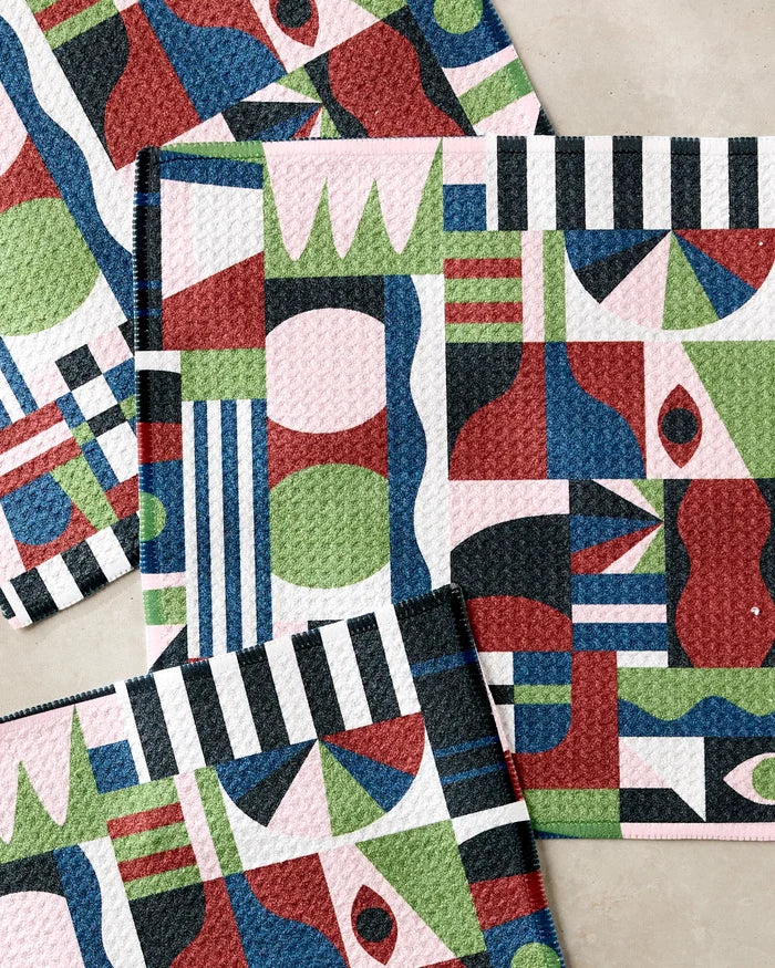 Four colorful, rectangular "Modern Bauhaus Mood" dishcloths by Claire Iglesias—featuring bold, abstract geometric patterns in red, green, blue, black, and pink with stripes, circles, and waves—overlap on a light surface.