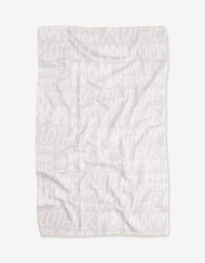 The GEOMETRY Mom blanket features white Geoweave fabric with repeated words MOM, MOTHER, and MOMMY in varied sizes and fonts in a light, semi-transparent print. The blanket is shown flat with some visible wrinkles.
