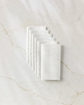 Seven white textured "Mom" reusable paper towels by GEOMETRY, featuring embossed text, are neatly stacked in an overlapping arrangement on a white marble surface with light brown veins.