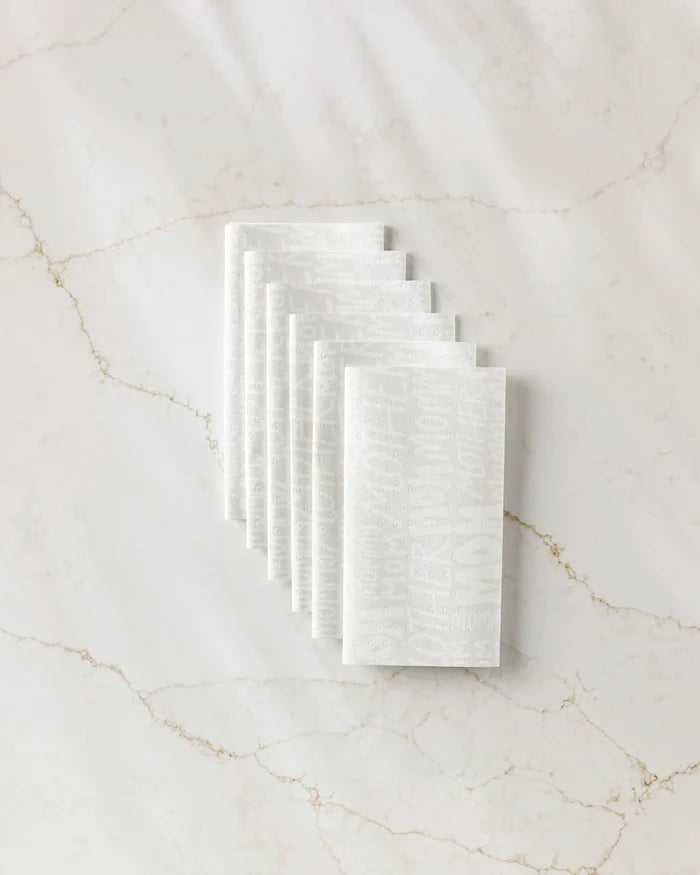 Seven white textured "Mom" reusable paper towels by GEOMETRY, featuring embossed text, are neatly stacked in an overlapping arrangement on a white marble surface with light brown veins.