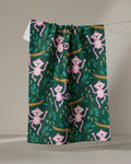 The "Monkeys" tea towel by Genna Blackburn, made from recycled materials, displays playful pink monkeys swinging among branches and leaves on a dark green background.