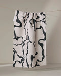 The Monochrome Liquid kitchen towel by Marina Solodka, cream-colored and recycled with abstract black squiggly lines, hangs from a string against a neutral background.